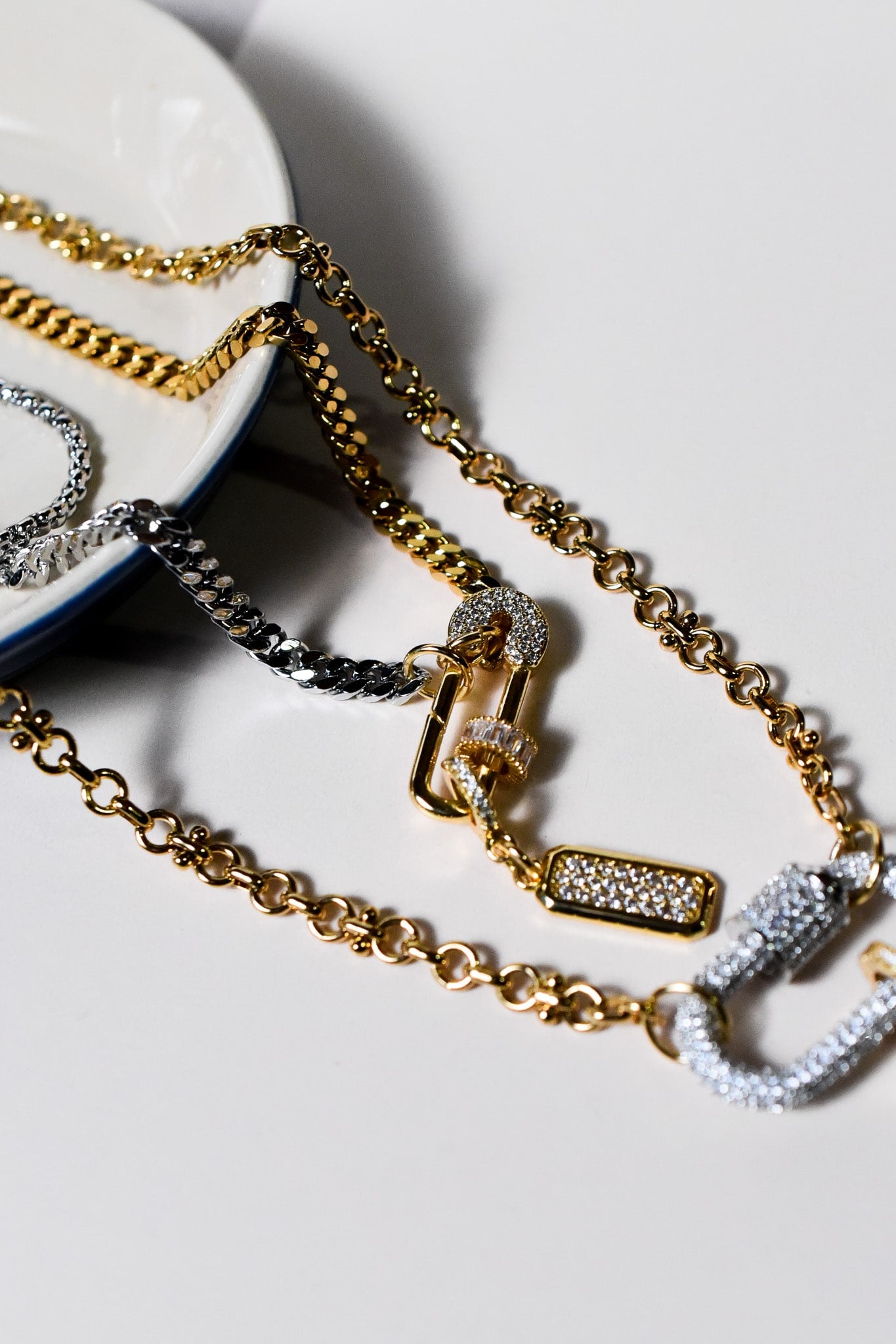 Detailed view of the INDIVIJWL Peacemaker necklace, showcasing a 24k gold plated CZ safety pin lock, silver carabiner, and 24k gold filled chains. A bold, customizable piece with a medium CZ pendant and removable charm holder.