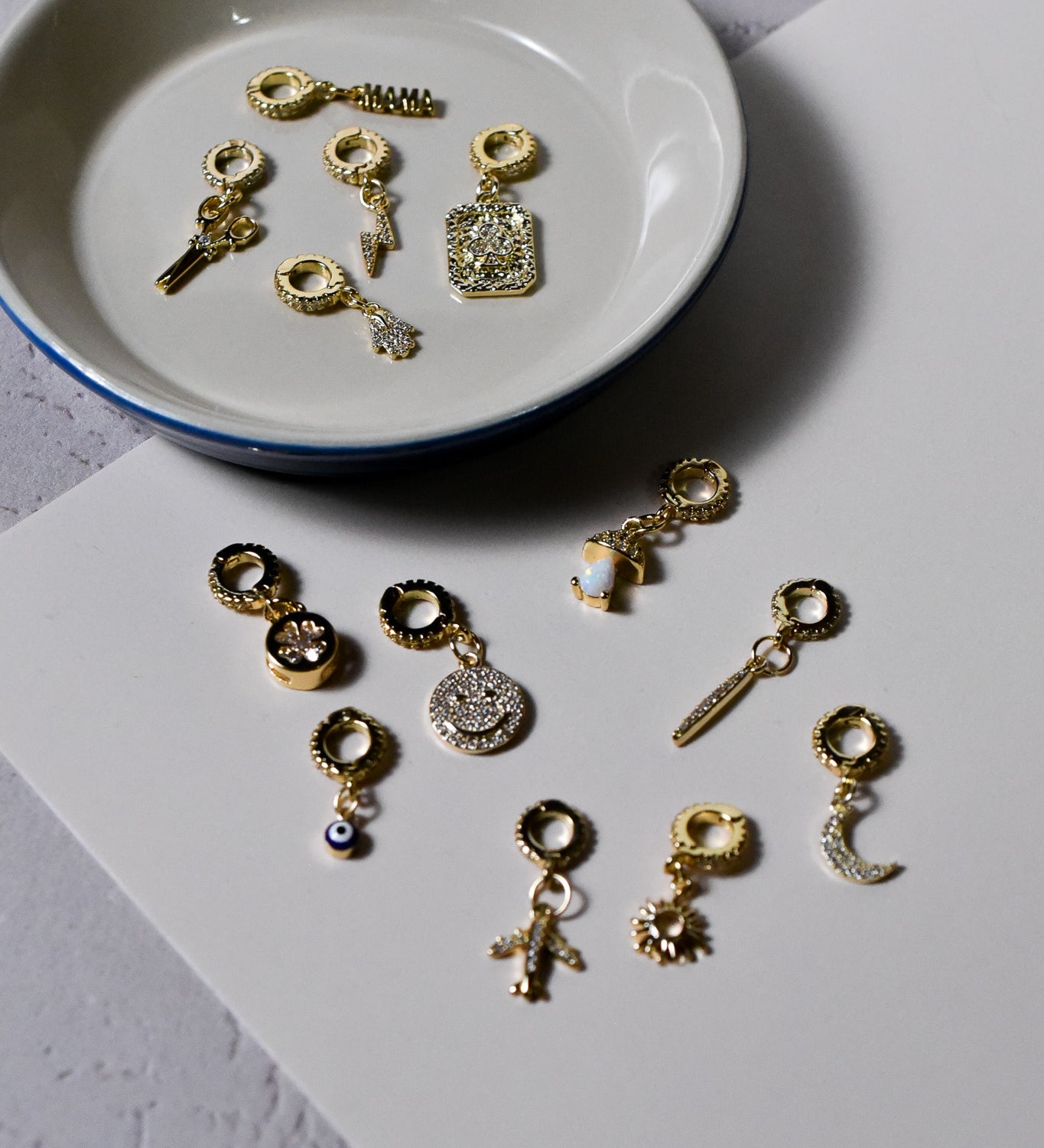 INDIVIJWL charm assortment showcasing various 14k gold-filled designs, including the crescent moon, smiley face, club pendant, and sword. Each charm includes micro-paved CZ details and removable 16k gold-filled bail clasps for effortless customization.