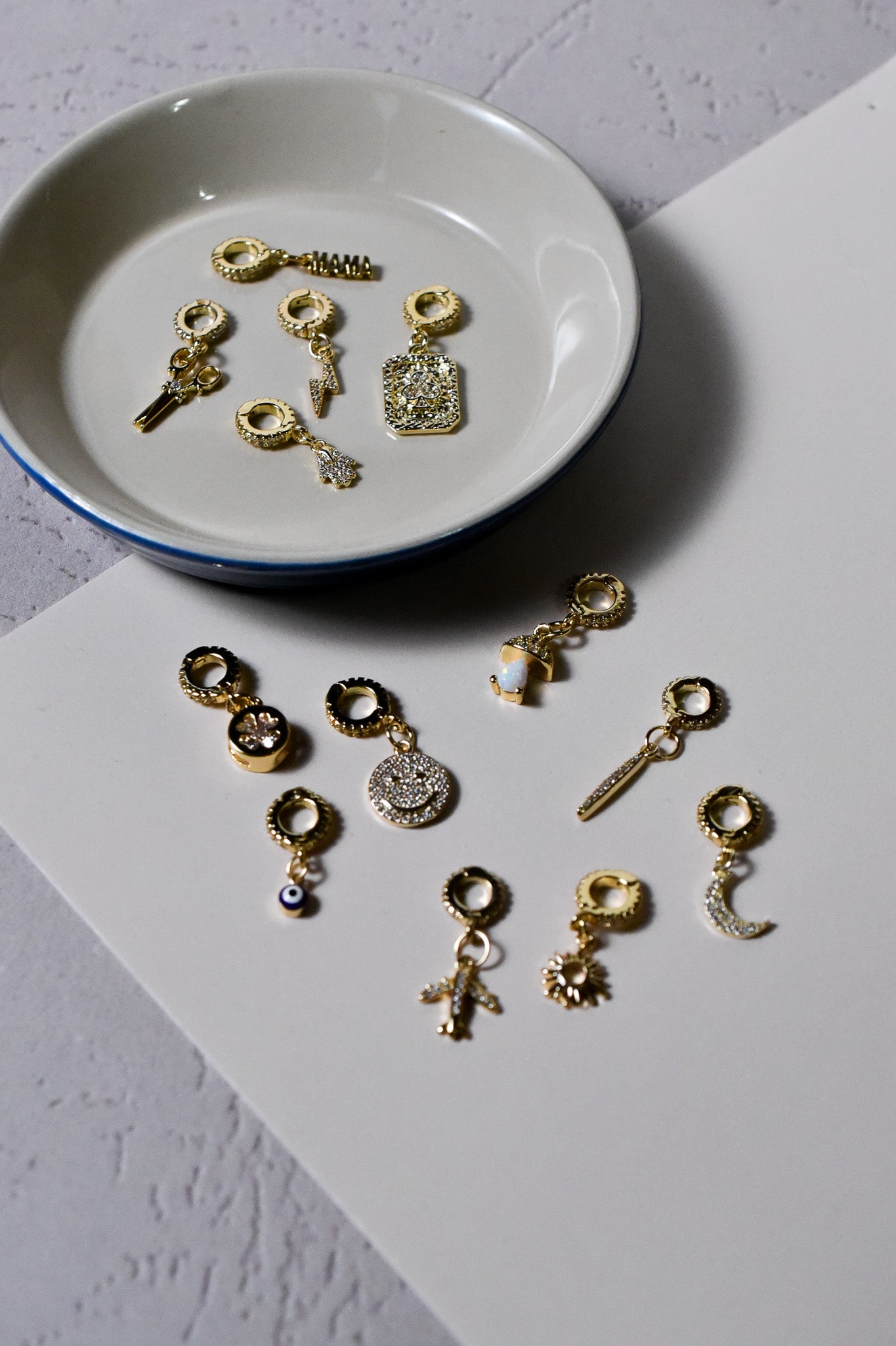 INDIVIJWL charm assortment showcasing various 14k gold-filled designs, including the crescent moon, smiley face, club pendant, and sword. Each charm includes micro-paved CZ details and removable 16k gold-filled bail clasps for effortless customization.