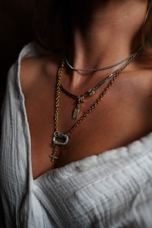 INDIVIJWL Peacemaker Stack on a model featuring a mixed metal safety pin lock necklace with 24k gold plated CZ over brass, a 16k gold filled removable charm holder, and a medium CZ pendant. Paired with a 21-inch 24k gold filled double rolo chain and a silver CZ carabiner lock with a 24k gold filled four-leaf petal charm for a bold, customizable layered look.